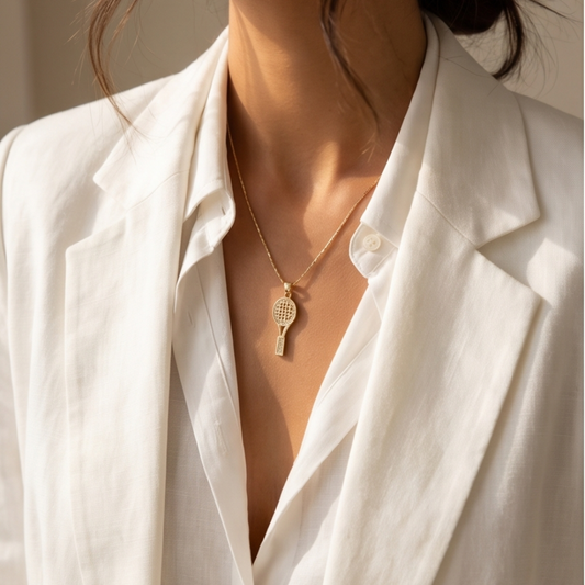 Person wearing a white blazer with a gold necklace featuring a tennis racket pendant.