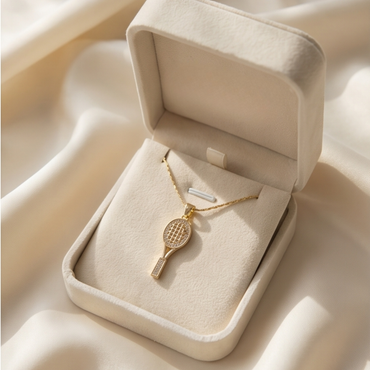 Gold necklace with a tennis racket pendant in an open jewelry box on a beige fabric background