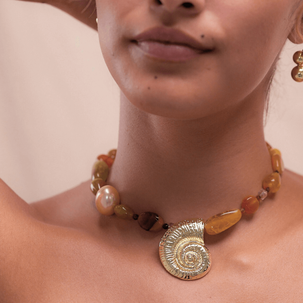Necklace with natural agate beads in warm tones and gold spiral shell pendant worn on model