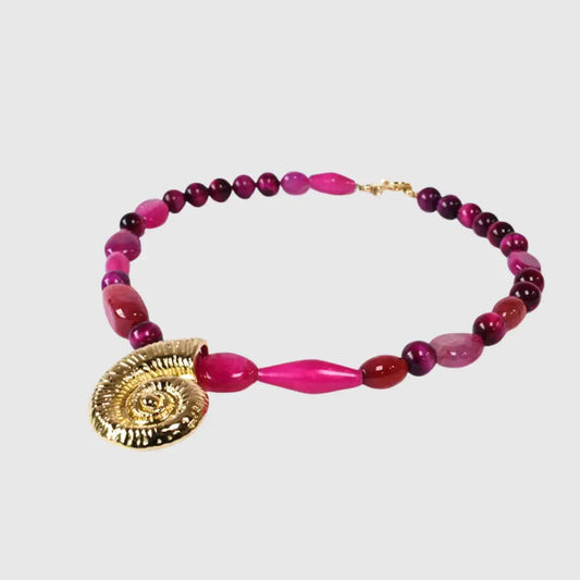 "Handcrafted necklace with vibrant fuchsia gemstone beads and gold spiral shell pendant – coastal statement jewelry for women"