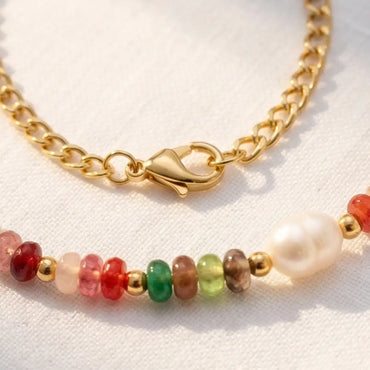 Close-up of gold chain anklet with colorful beads and pearl detail showing texture and design