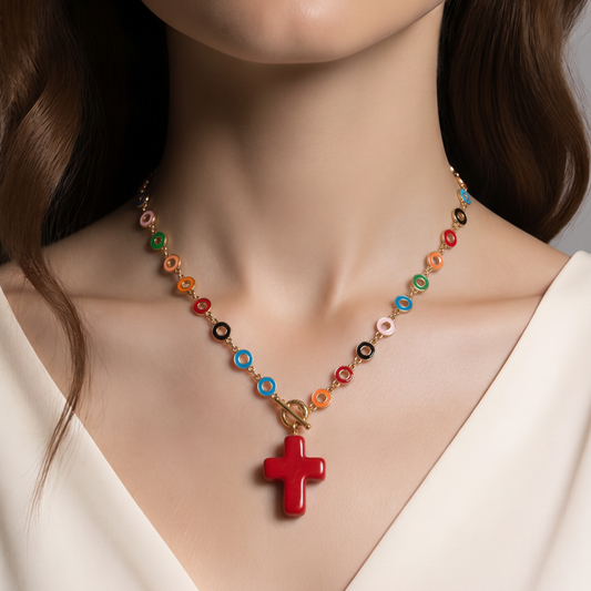A close-up of a model wearing a colorful beaded necklace with a red cross pendant. The necklace features gold-toned links and small circular beads in multiple colors including orange, green, blue, pink, and black.