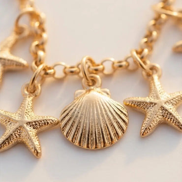 close up of gold anklet with starfish and shell charms detailed summer beach jewelry design