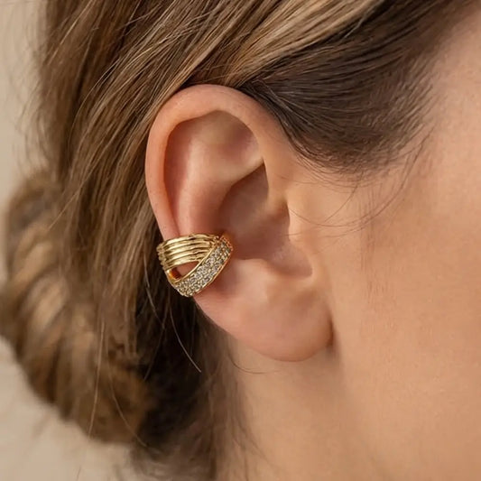 Gold ear cuff with gemstones worn by a person with brown hair.