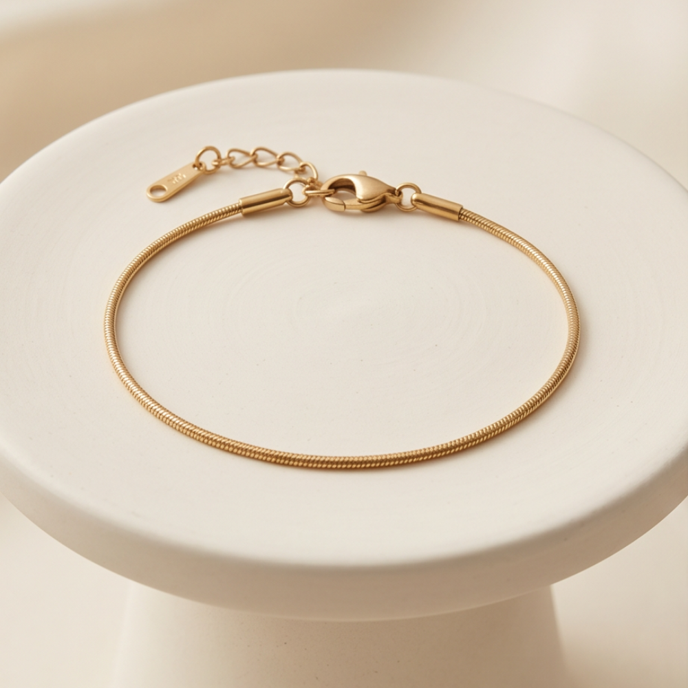 Gold bracelet on a white pedestal with a beige background