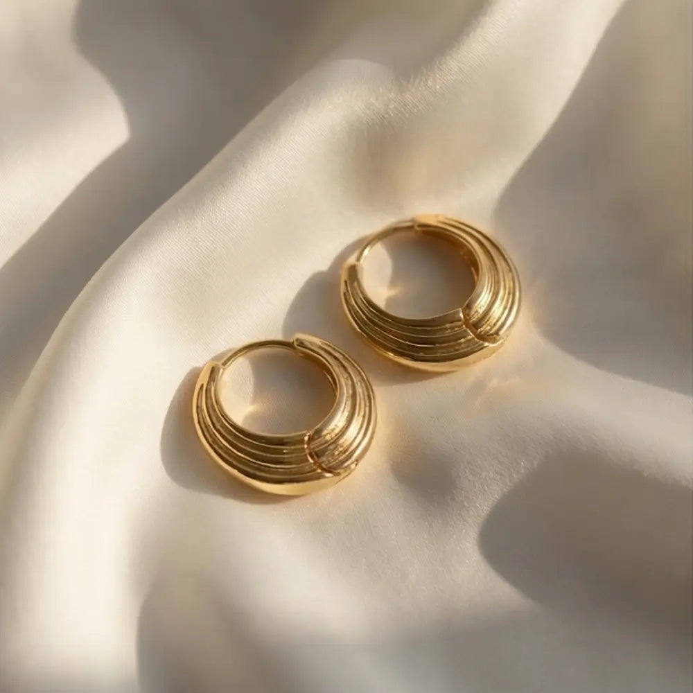 layered gold hoop earrings ribbed chunky design on soft fabric background