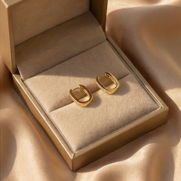 Gold hoop earrings in an open jewelry box on a beige fabric background
