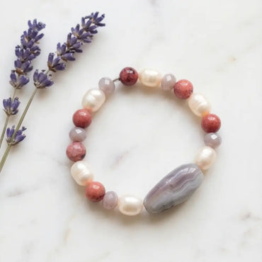 Beaded bracelet with purple, pink, and gray stones on a marble surface with lavender flowers.