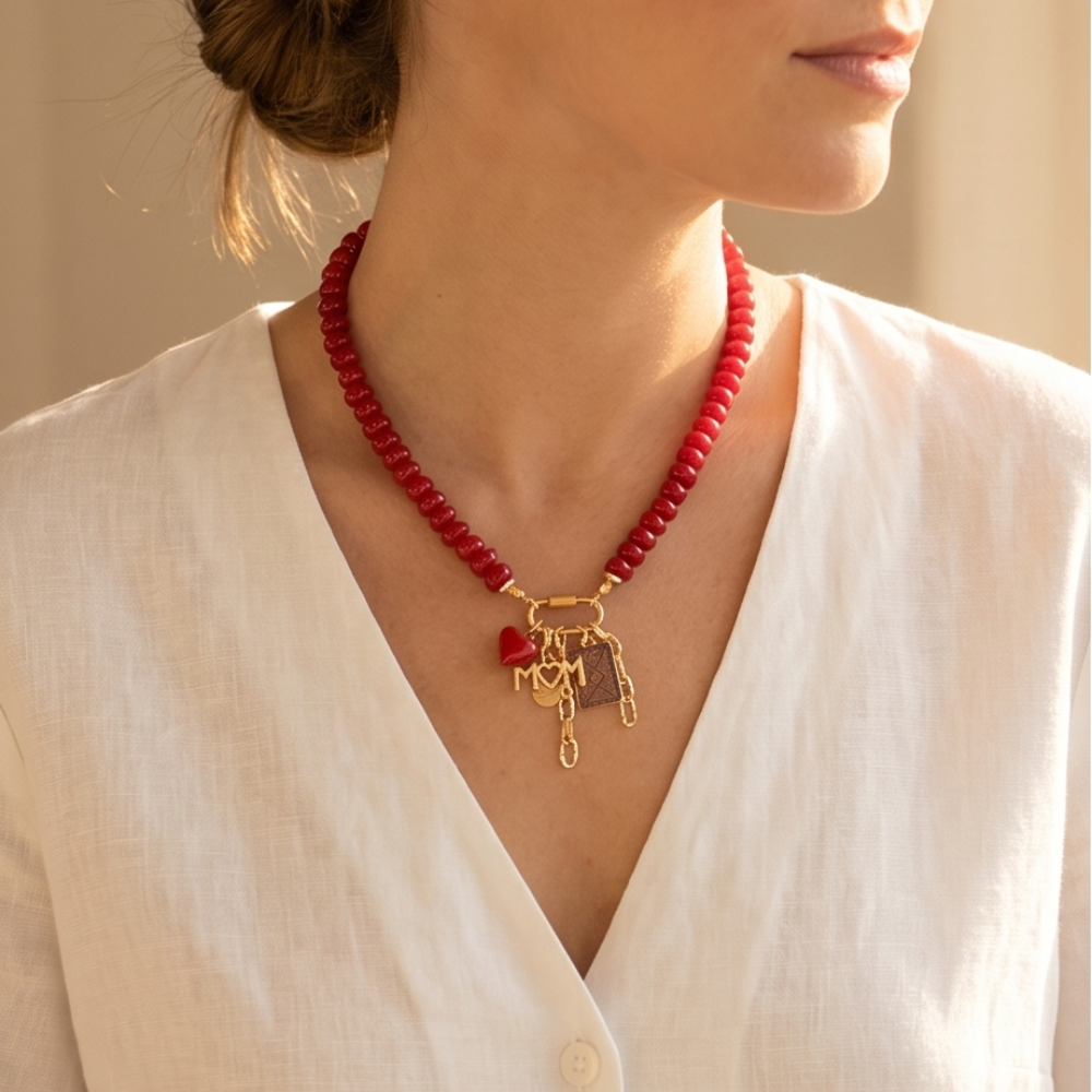 Red beaded necklace with gold charms worn by a person in a white shirt.