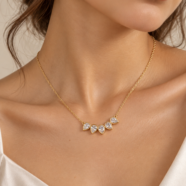 Close-up of a woman wearing the Petal Bezel Necklace by Julie Saldivia, featuring five sparkling pear-shaped clear stones set in 18K gold-plated 925 sterling silver. Delicate adjustable 15–18 inch necklace styled with an elegant ivory satin top.