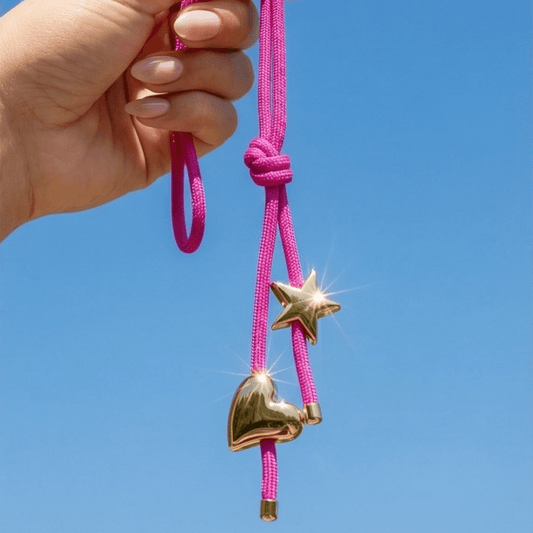 Hand holding a pink cord with gold heart and star charms against a clear blue sky