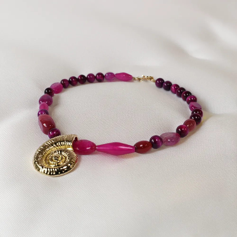 "Handcrafted necklace with vibrant fuchsia gemstone beads and gold spiral shell pendant – coastal statement jewelry for women"