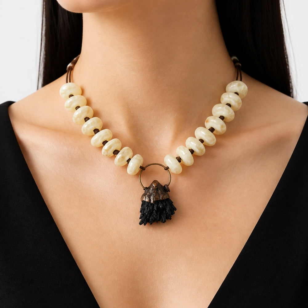 A close-up of a model wearing a statement necklace made of cream-colored stone beads and a dark mineral cluster pendant.