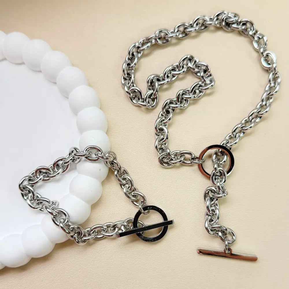 Silver chain necklace with a white beaded bracelet on a beige background