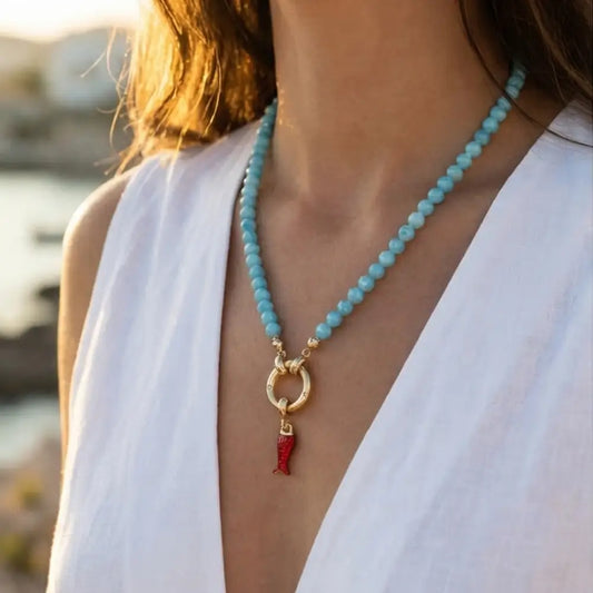 turquoise beaded necklace with gold clasp and red charm on table lifestyle jewelry Julie Saldivia