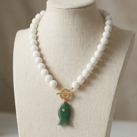 White beaded necklace with green fish pendant on display bust modern elegant jewelry