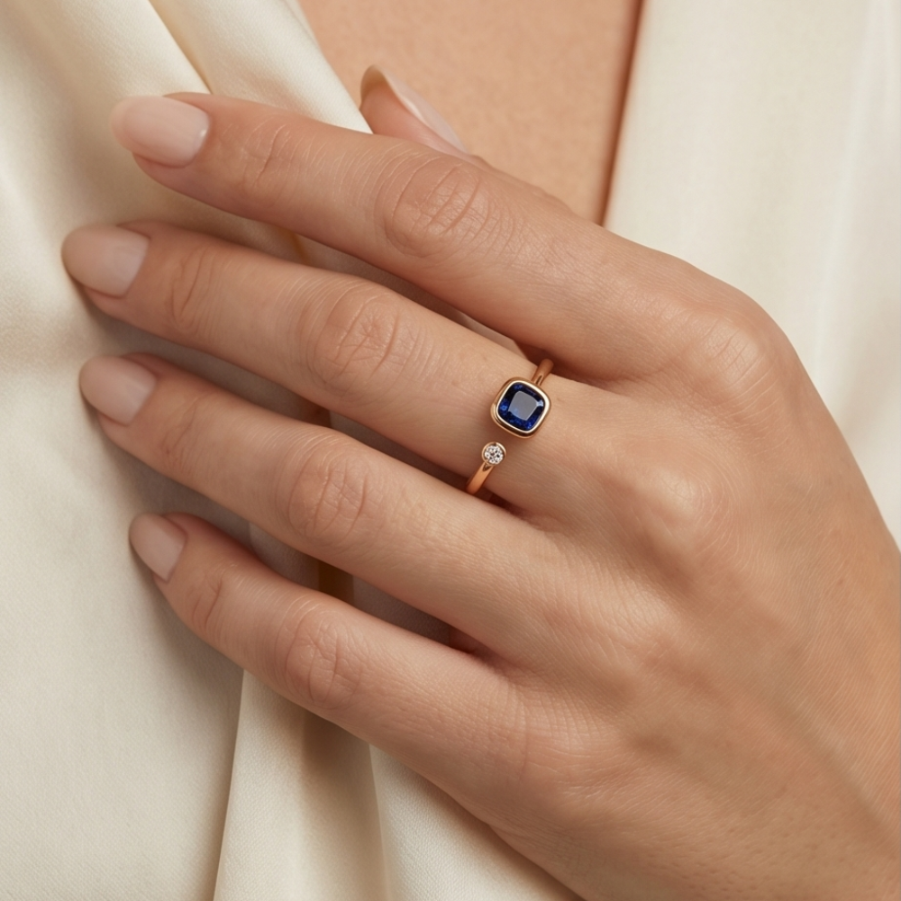 Hand wearing a ring with a blue gemstone on a light background