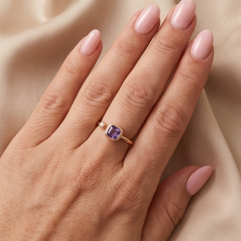 Hand wearing a gold ring with a purple gemstone on a beige fabric background