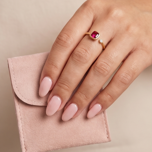 Hand wearing a gold ring with a red gemstone on a beige background
