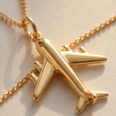 Gold airplane pendant on a chain against a beige background