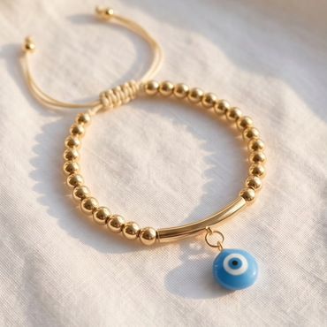 Gold bracelet with a blue evil eye charm on a white fabric background