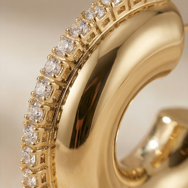 Gold earring with clear gemstones on a beige background