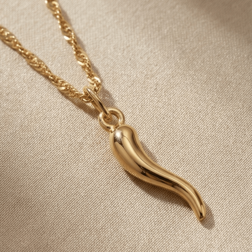 Gold chili pepper pendant necklace on a beige fabric background