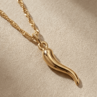 Gold chili pepper pendant necklace on a beige fabric background