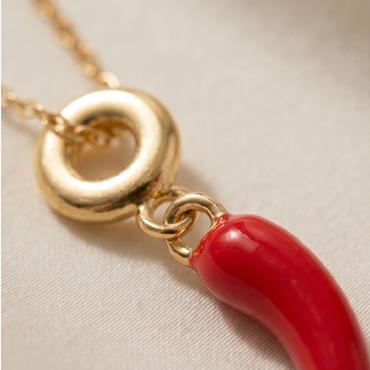 Gold necklace with a red pendant on a beige background