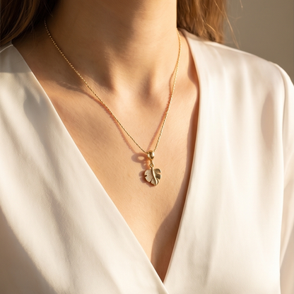 Gold necklace with a leaf pendant worn by a person in a white outfit.