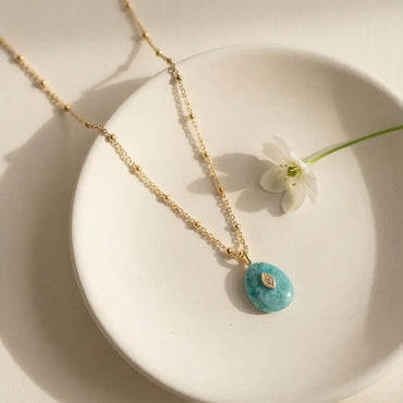 Minimal gold necklace with amazonite pendant styled on neutral plate with soft light
