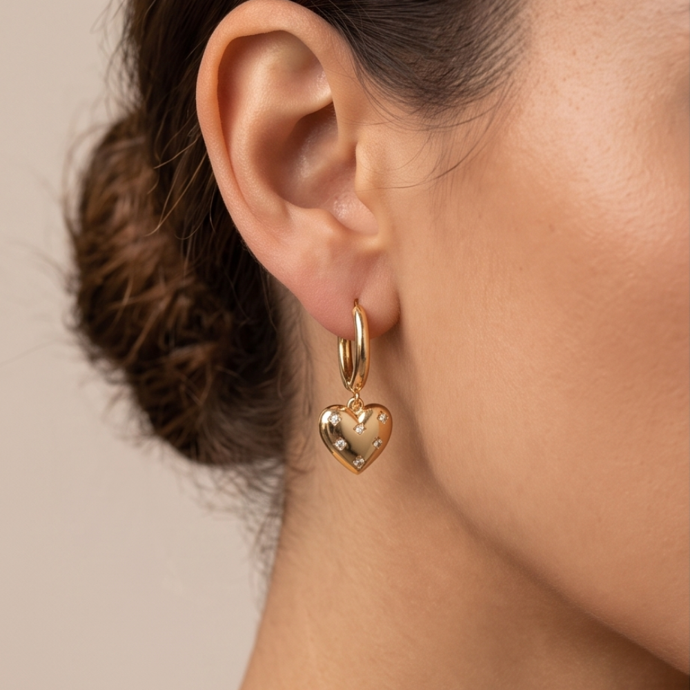 Model wearing an Amour gold-tone hoop earring with a dangling heart charm and clear accents.