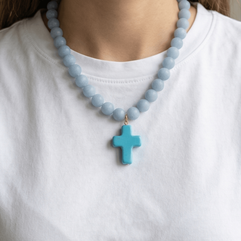 Woman wearing an 18-inch angelite beaded necklace with a blue enamel cross pendant.