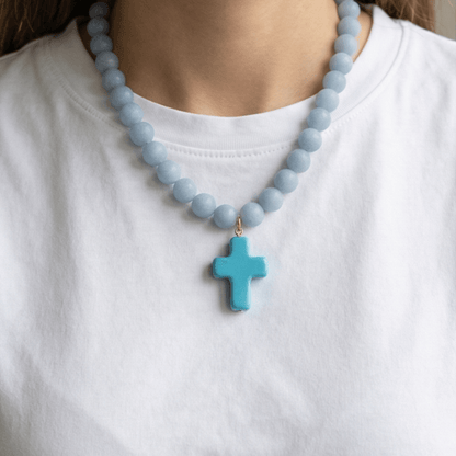 Woman wearing an 18-inch angelite beaded necklace with a blue enamel cross pendant.
