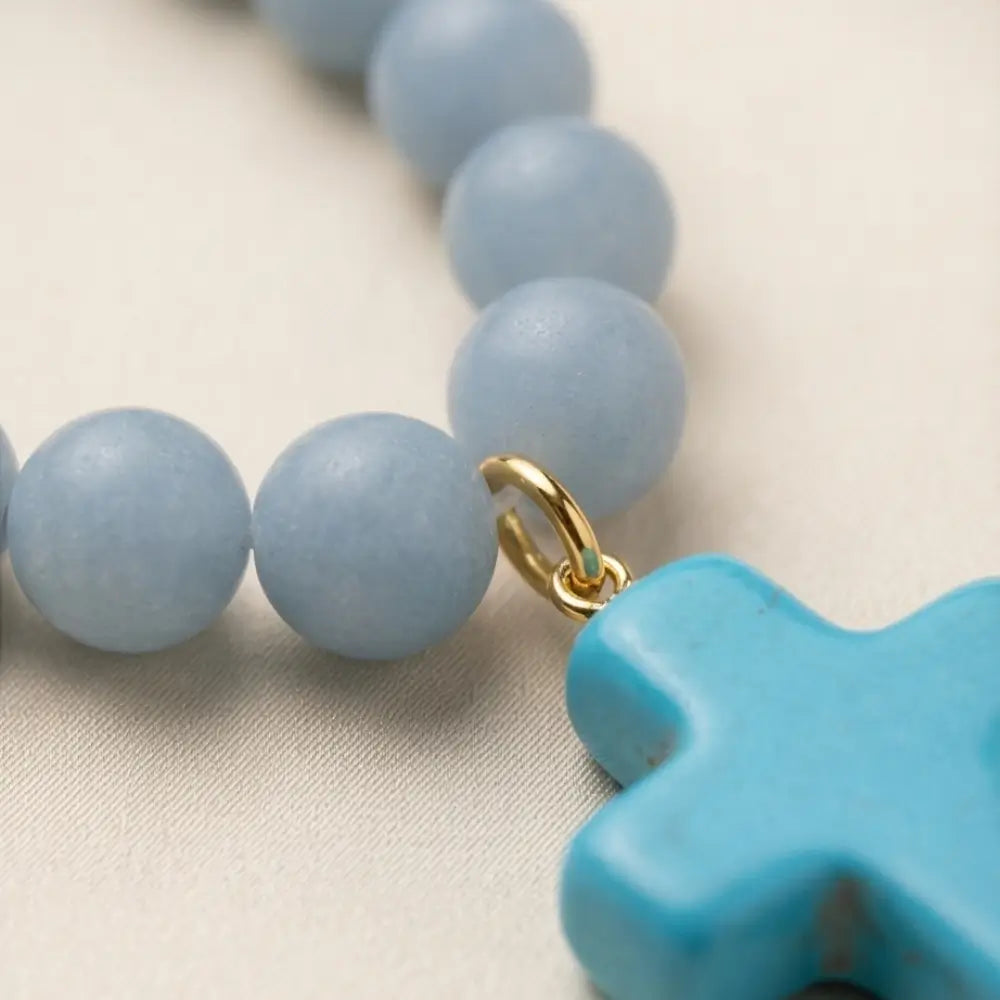 Close-up of angelite stone beads with a blue enamel cross pendant and gold-tone connector.