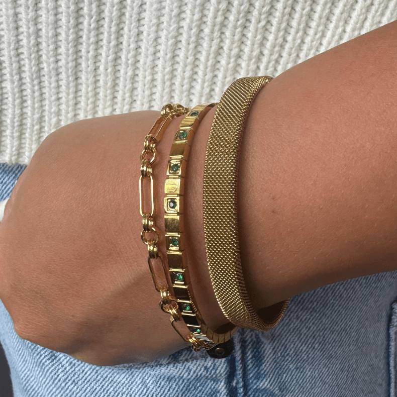 A gold bangle bracelet made of high-quality stainless steel, featuring green rhinestones and an adjustable fit for wrist sizes from 6 to 9 inches. The bracelet is displayed on a light background, highlighting its sleek and elegant design. Ideal for adding a touch of sophistication to both professional and casual outfits, suitable for business women aged 35-60.