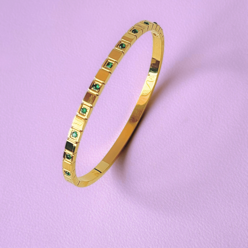 A gold bangle bracelet made of high-quality stainless steel, featuring green rhinestones and an adjustable fit for wrist sizes from 6 to 9 inches. The bracelet is displayed on a light background, highlighting its sleek and elegant design. Ideal for adding a touch of sophistication to both professional and casual outfits, suitable for business women aged 35-60.