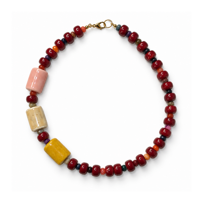 Bordeaux beaded necklace with three oversized blush, cream and ochre beads arranged asymmetrically on one side.