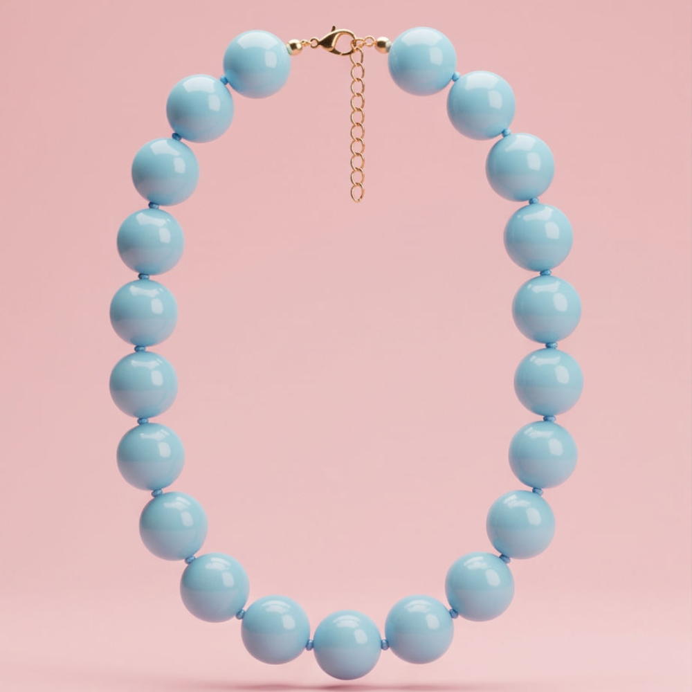A light blue beaded necklace with a gold clasp and extender chain, displayed against a solid pink background.