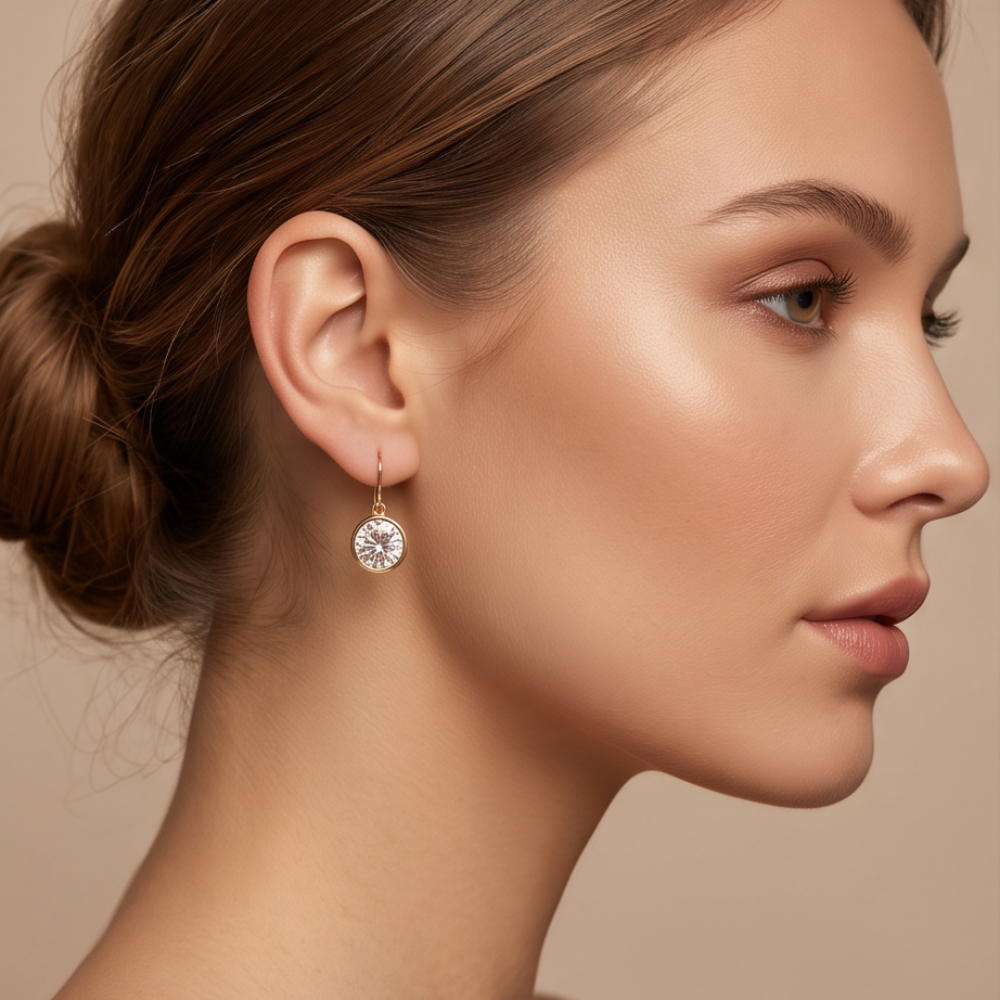 Model wearing a Clara gold-tone drop earring with a clear round faceted accent.