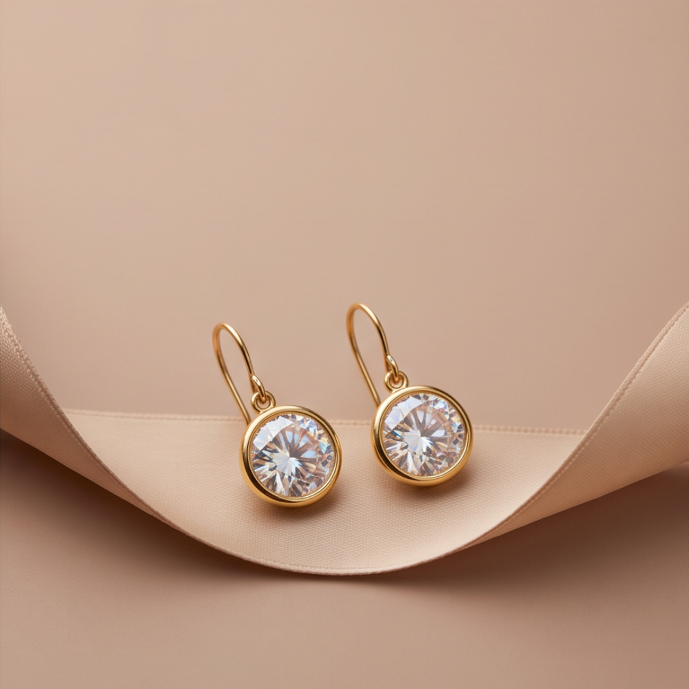 Pair of Clara gold-tone bezel drop earrings displayed on a cream jewelry stand.
