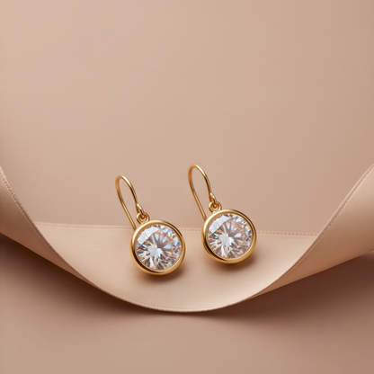 Pair of Clara gold-tone bezel drop earrings displayed on a cream jewelry stand.