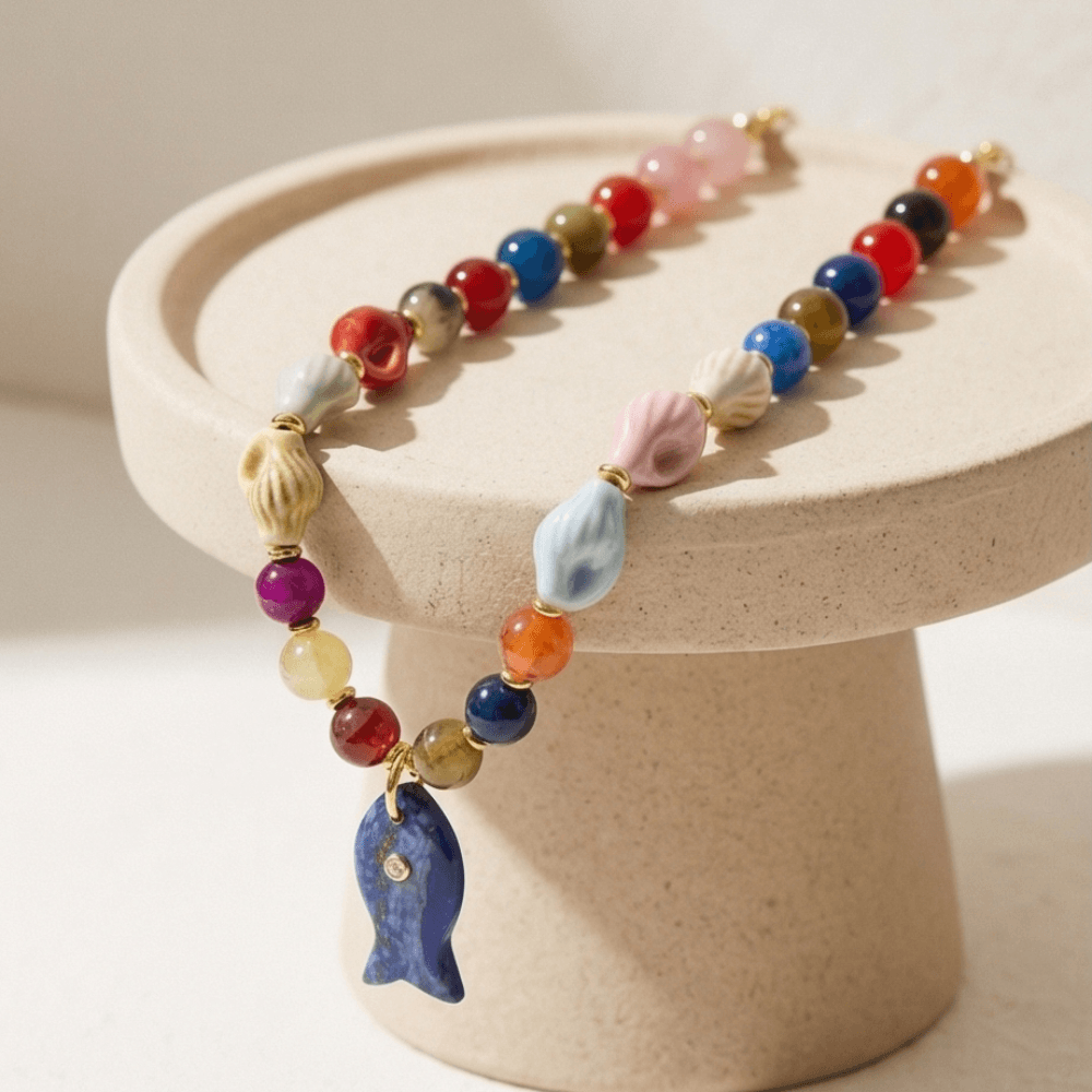Colorful gemstone necklace displayed on ceramic stand with fish pendant