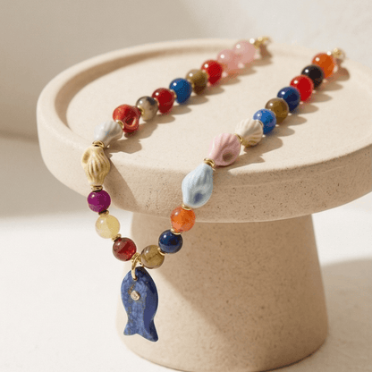 Colorful gemstone necklace displayed on ceramic stand with fish pendant