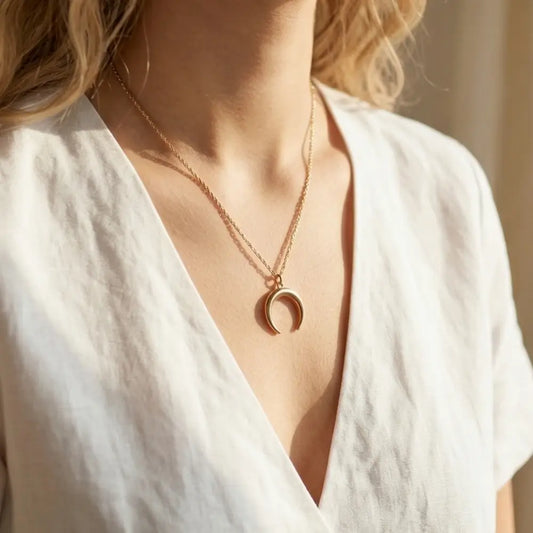 Gold necklace with a crescent moon pendant worn by a person in a white top.