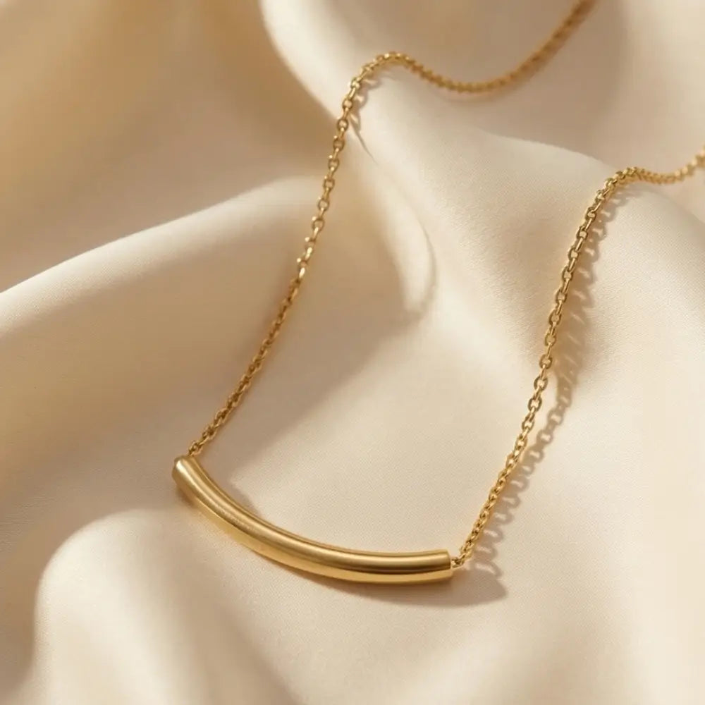 Close up of curved gold bar necklace on soft fabric minimal jewelry design