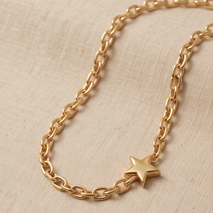 A gold chain necklace with a small star charm, displayed on a textured beige linen fabric background.