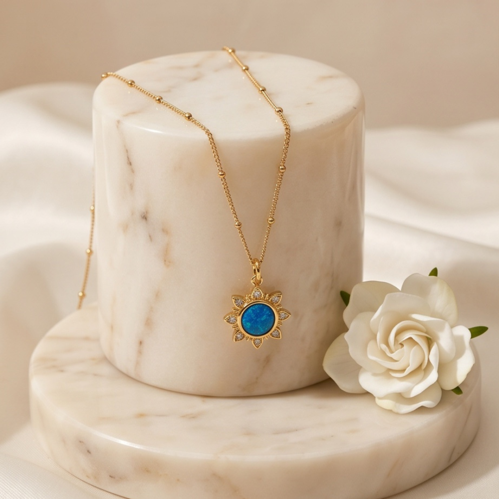 Gold blue opal sun pendant necklace displayed on marble stand with white rose