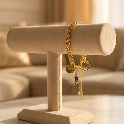 Gold chain charm bracelet with love pendant and blue fish charm displayed on jewelry stand by Julie Saldivia Jewelry