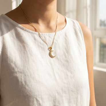 Person wearing a gold necklace with a moon pendant in a softly lit room.
